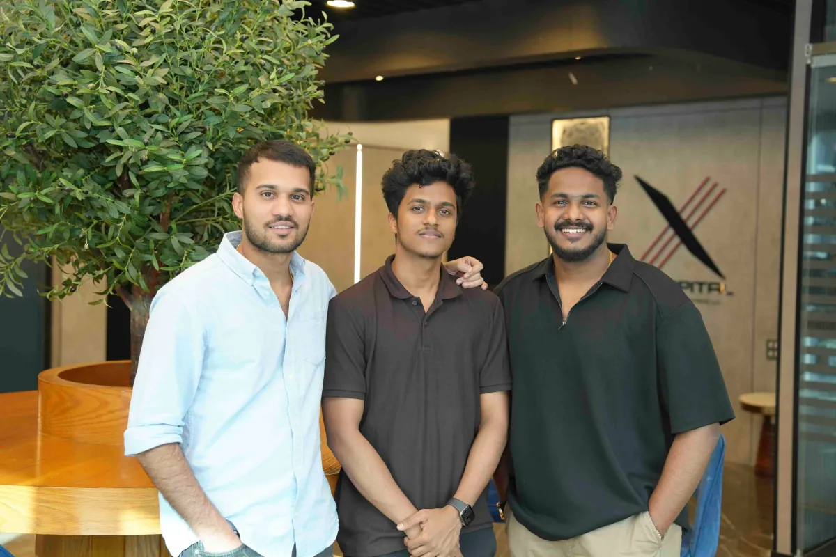 Three members of the 3X Studio team in the office, beside the 3X Capital logo wall